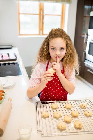 Curly-Haired Girl in Red Apron Baking Cookies in Kitchen