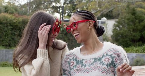Friends laughing in red novelty glasses wearing cozy knit sweaters in garden