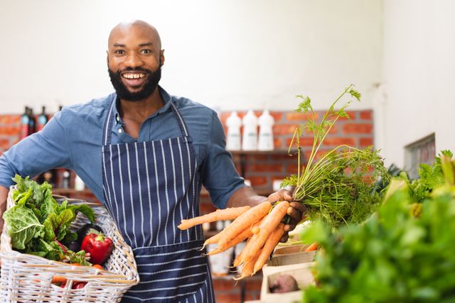 African American vendor smiling while holding fresh vegetables in a store. Ideal for use in articles or advertisements about organic food, healthy eating, small businesses, and local markets. Perfect for promoting sustainable agriculture, retail stores, and entrepreneurship.