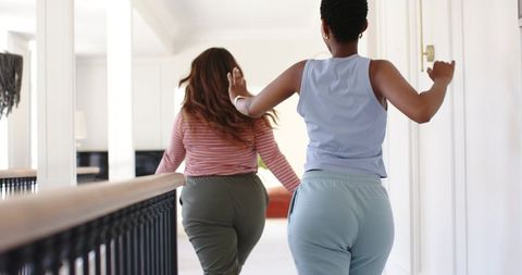 Two women walking down bright upstairs hallway wearing loungewear holding banister
