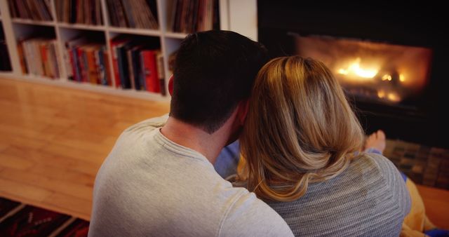 Couple relaxing together by a warm fireplace at home with a view of a bookcase in the background. great for promoting romance, home insulation products, cozy winter scenes, or lifestyle blogs featuring relationship tips and home decor ideas.