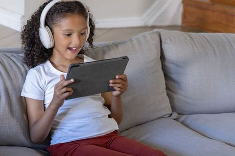 African american girl enjoying tablet with wireless headphones on living room couch