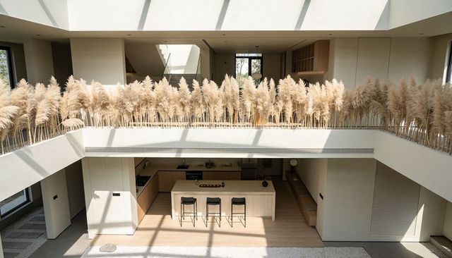 Pampas grass-lined mezzanine framing sunlit modern atrium with timber kitchen island