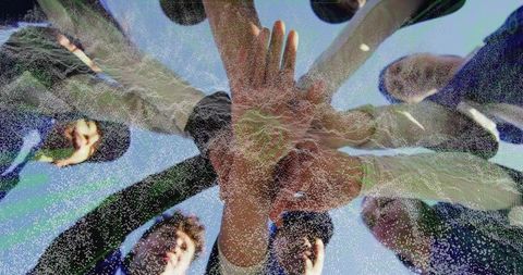 Female athletes stacking hands in team huddle under clear sky