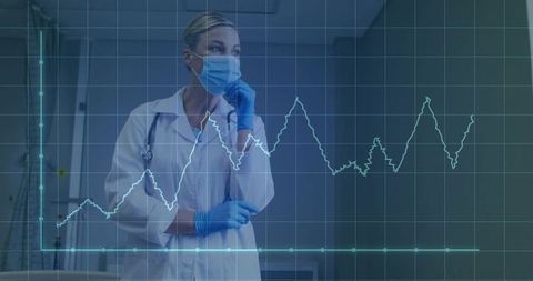 Female clinician assessing cardiac rhythm on monitor in hospital corridor with ppe