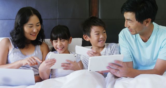 Family bonding and enjoying tech devices together on bed in the morning, perfect for family lifestyle, technology use, or weekend leisure activities advertising. Can be used in promotions for family gadgets, online learning, or digital lifestyle content.