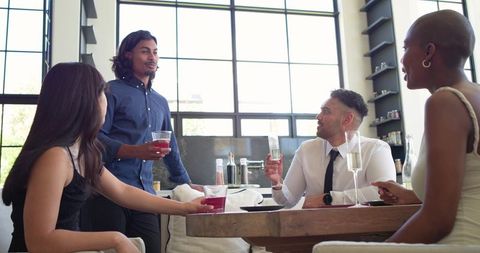 Loft kitchen friends gathering around table toasting drinks in sunlit open-plan interior