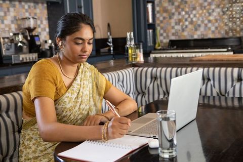 Indian woman in sari writing in notebook at cafe workstation