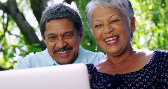A senior African American couple shares a joyful moment while looking at a laptop screen, with copy space. Their smiles suggest they are enjoying leisure time, connecting with loved ones or engaging in a fun activity online.
