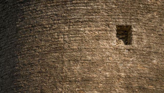 Weathered curved stone tower wall with small square opening, textured masonry detail