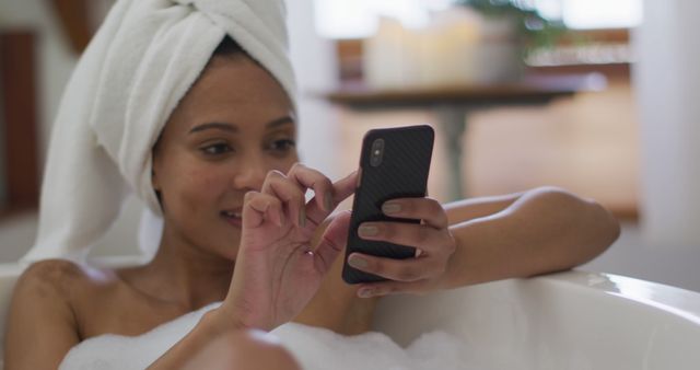 Biracial woman taking a bath and using smartphone. domestic life, spending quality free time relaxing at home.