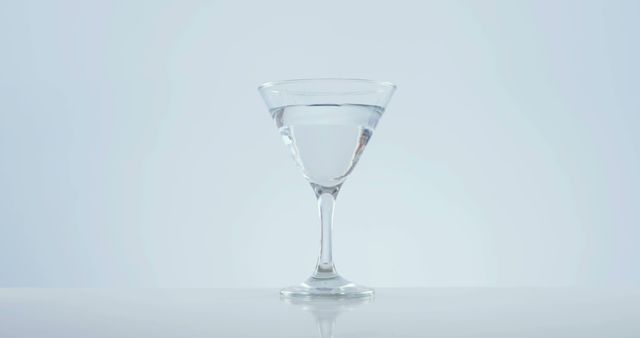 A clear martini glass filled with a transparent liquid stands against a light background, with copy space. Its elegant design suggests a sophisticated setting, ideal for concepts related to fine dining or celebratory events.