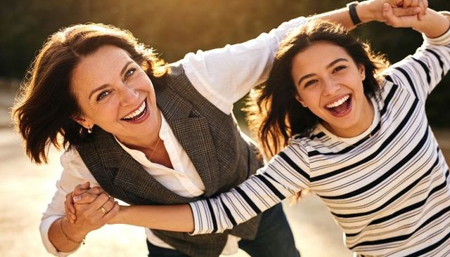 Mother daughter laughing at golden hour while holding hands on sunlit pavement