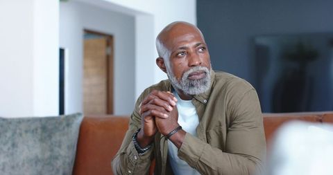 Mature man reflecting while sitting on leather sofa in modern living room