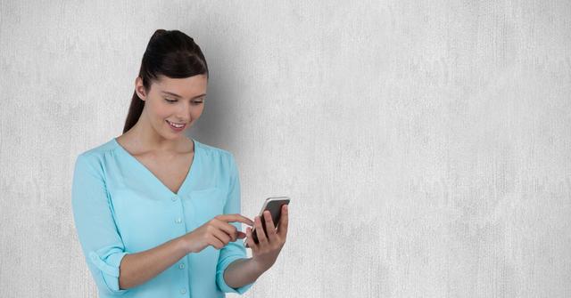 Smiling woman wearing blue shirt using smartphone against gray background. Ideal for depicting modern technology, communication, social media engagement, or casual digital interactions.