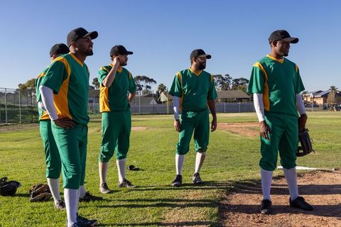 Sunlit baseball team standing on infield wearing green and yellow uniforms holding gloves