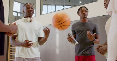 Young black men chatting tossing basketball on indoor gym sideline showing camaraderie