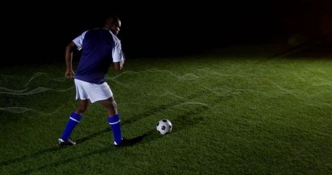 Soccer player preparing shot on night turf with ball, dramatic lighting and copy space