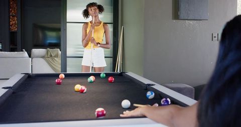 Two african american women playing pool in modern home rec room casual leisure