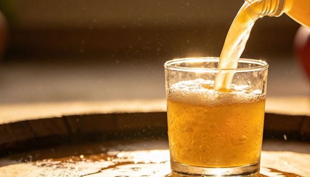 Pouring golden beer into tumbler over wet wooden barrel with backlit foam