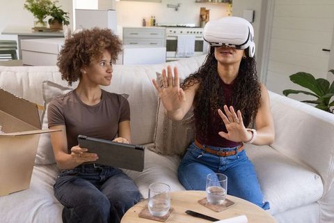 African american women exploring virtual reality on sofa while using tablet in modern home