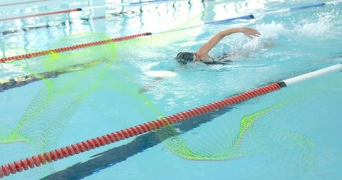 Woman swimmer performing freestyle in indoor lap pool passing lane ropes creating splash reflections