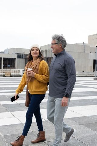 Middle-aged couple walking urban plaza holding coffee and smartphone casual autumn style