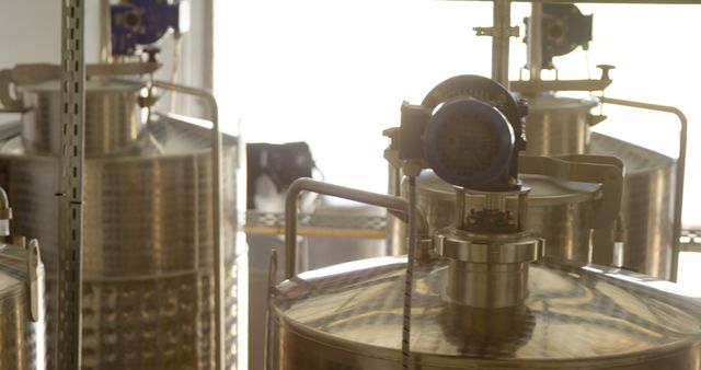 This image shows stainless steel tanks in a craft brewery, reflecting sunlight. Ideal for use in articles about brewing process, craft beer industry, industrial equipment, or small-scale production.