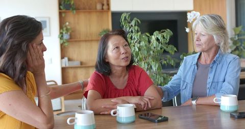 Asian woman receiving comfort from diverse friends around wooden dining table
