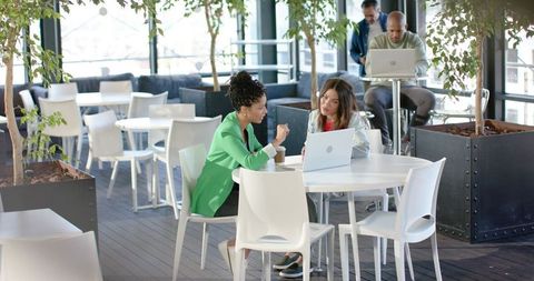 Diverse professionals collaborating in sunlit coworking cafe over laptop and coffee