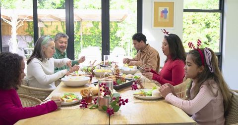 Multigeneration family sharing festive holiday meal around sunlit rustic wooden dining table