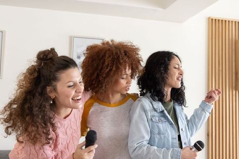Diverse friends singing together in cozy living room holding microphones enjoying karaoke