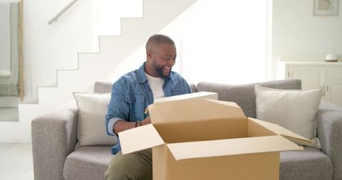 Happy african man unboxing home decor on sofa enjoying new delivery and joyful surprise