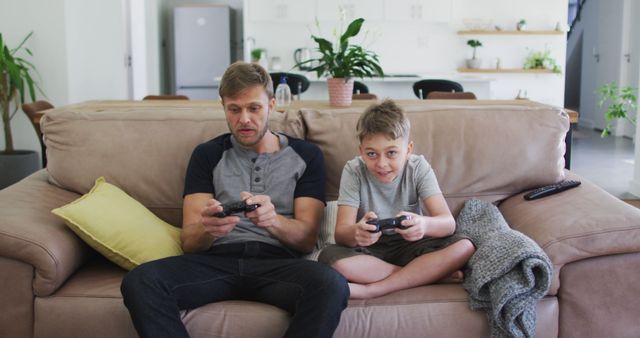 Father and son playing video games together on living room couch - Download Free Stock Images Pikwizard.com