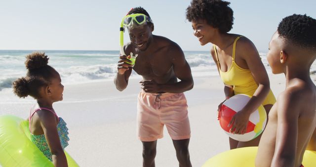 Family spending quality time on sunny beach, wearing swimwear, enjoying day with floaties and beach ball. Perfect for concepts related to family vacations, summer fun, children enjoying outdoors, and bonding time.