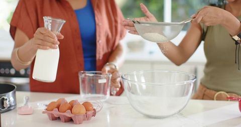 Indian and african american women baking together sifting flour pouring milk