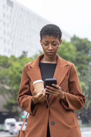 African american professional checking smartphone while holding coffee cup on city commute