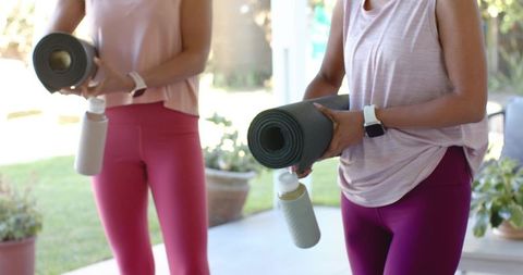 Diverse women in pink athleisure holding yoga mats and water bottles on sunlit patio