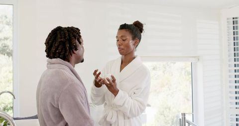 African american couple applying moisturizer in sunlit modern bathroom for morning skincare