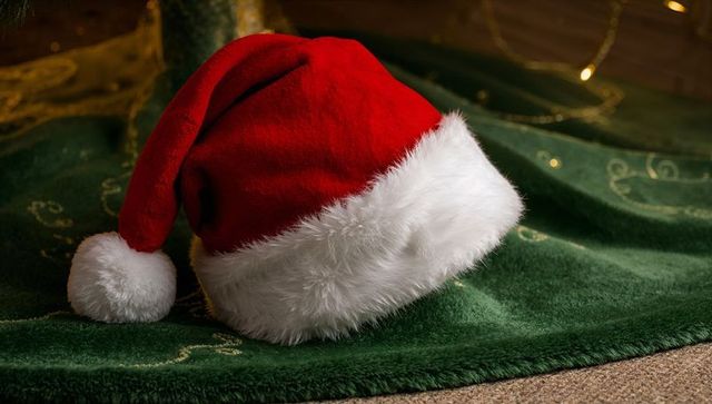 Resting santa hat on green tree skirt showing plush fur trim and warm holiday lights