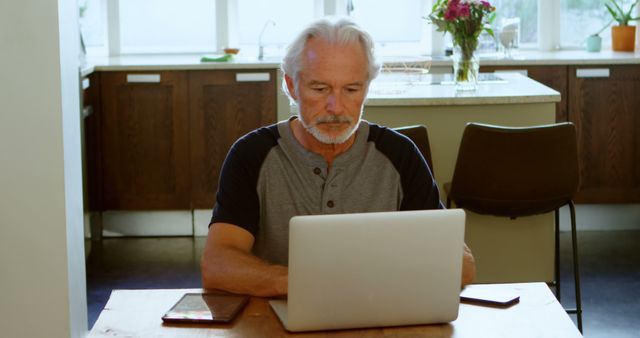 Senior man working on computer at home kitchen table - Download Free Stock Images Pikwizard.com