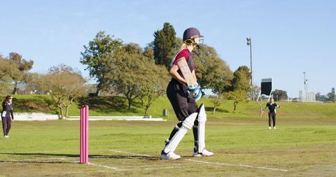 Teenage Girl Cricket Player Holding Bat on Field by Pink Stumps