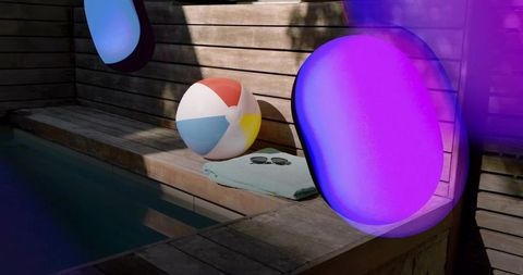 Glowing purple-blue led float casting color on sunlit poolside bench with beach ball