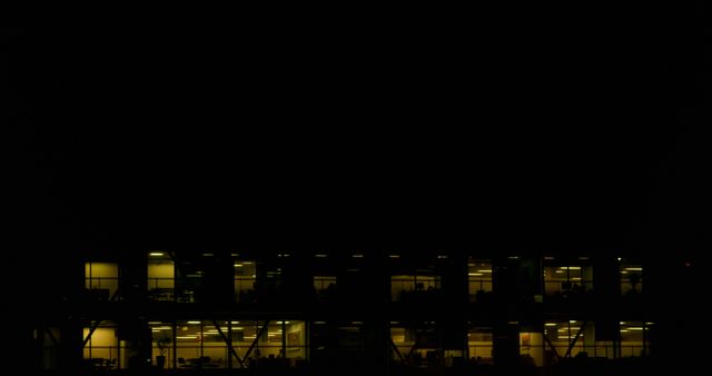 Dimly-lit office windows from a distance, showcasing late-night work culture. Suitable for themes of corporate life, urban night scenes, office environments, business concepts, and work-life balance contexts.