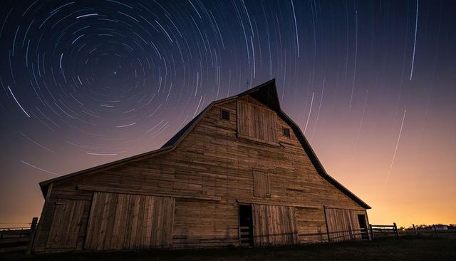 Rustic wooden barn under circular star trails night sky long exposure rural landscape
