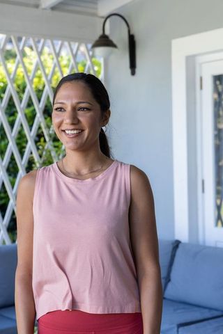 Smiling african american woman on covered porch in pink sleeveless top and red leggings