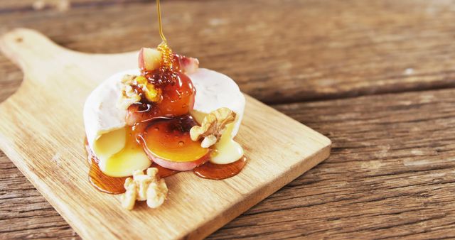 Honey drizzles over a slice of fig and a creamy cheese topped with walnuts on a wooden board, with copy space. This appetizing setup suggests a gourmet experience with a focus on fresh and natural ingredients.