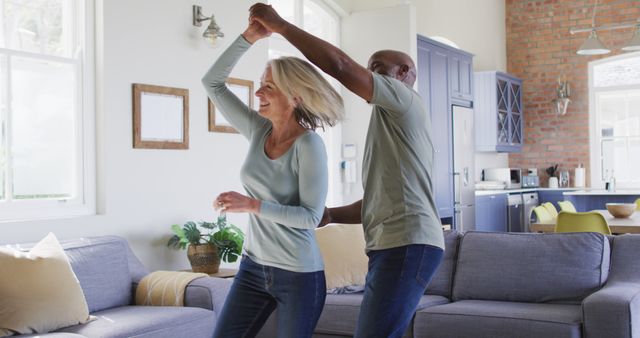 Mature couple dancing in bright modern living room, expressing happiness and togetherness. Their casual attire and joyful expressions make this a heartwarming capture, perfect for illustrating themes related to love, retirement, lifestyle bonding, and enjoying moments at home. Suitable for use in advertisements, lifestyle blogs, interior design inspirations, or relationship articles.