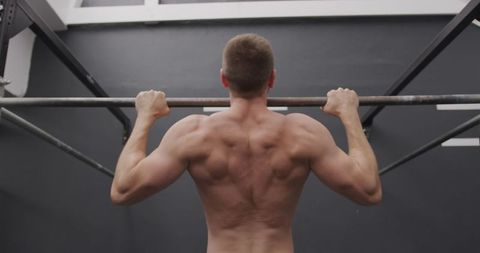 Shirtless Man Performing Chin Ups in Gym for Strength Training