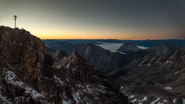 Panoramic view of the Zugspitze mountain range during sunrise, showcasing the golden hue on the highest peak in Germany. Ideal for travel guides, nature photography collections, landscape posters, and adventure blogs highlighting the beauty of alpine regions.